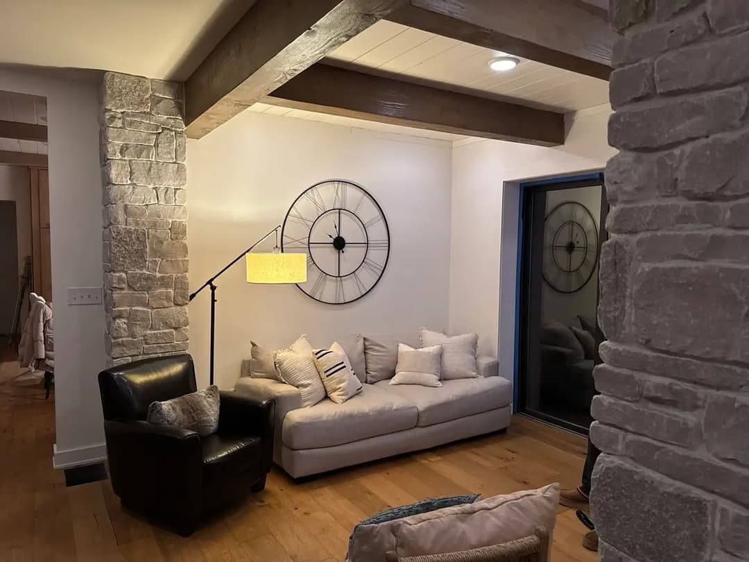 Cozy living room with stone walls, modern clock, and minimalist furniture.