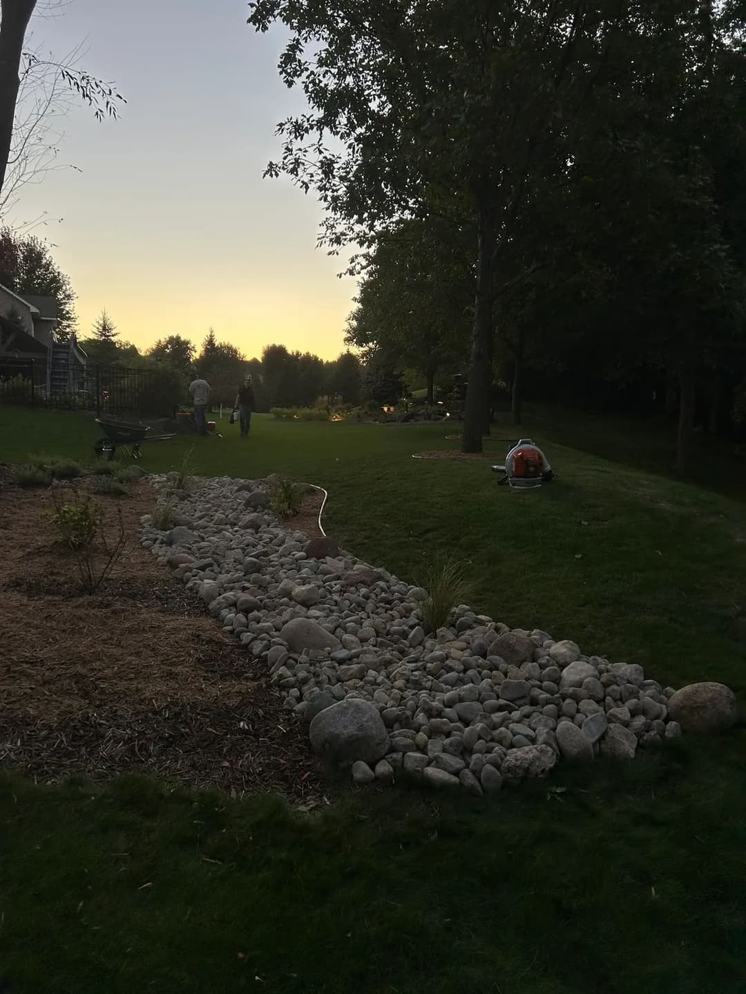 Landscape at sunset features a stone path, garden beds, and people working in a serene setting.