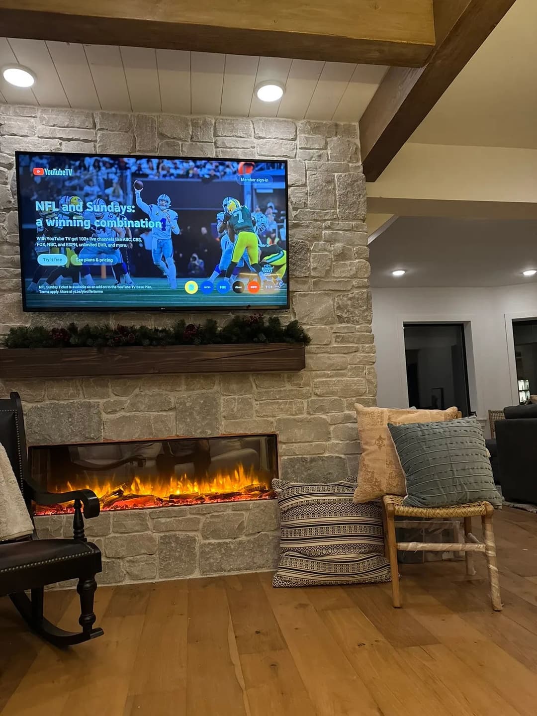 Cozy living room with a TV displaying NFL content above a stone fireplace and decorative pillows.