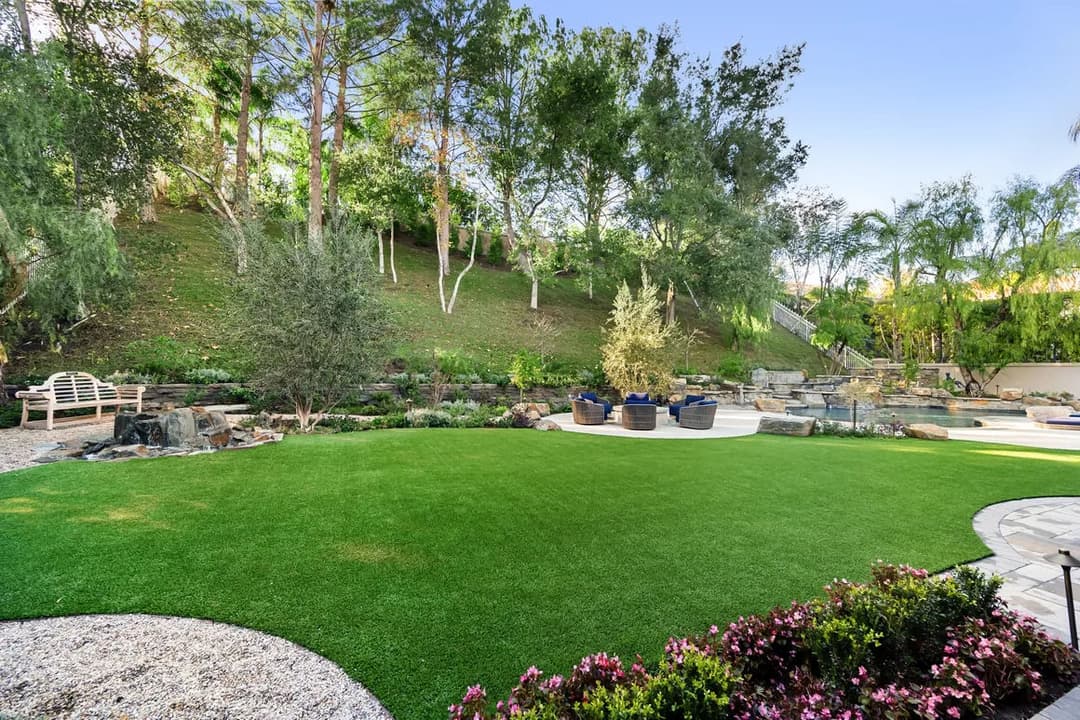 Lush landscaped yard with artificial grass, trees, and outdoor seating area.