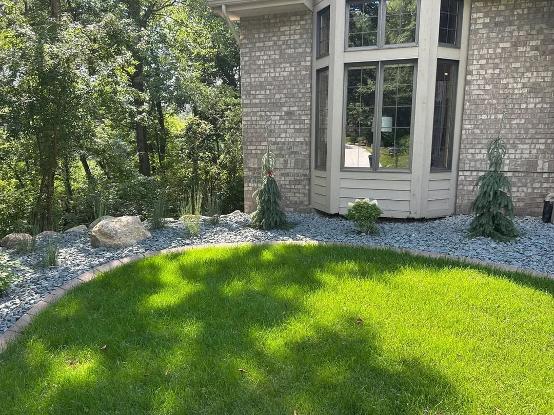 Landscape featuring a well-manicured lawn, decorative stones, and shrubs near a modern home.