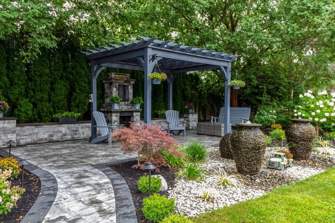 Elegant garden with a pergola, seating area, and decorative stone features surrounded by greenery.