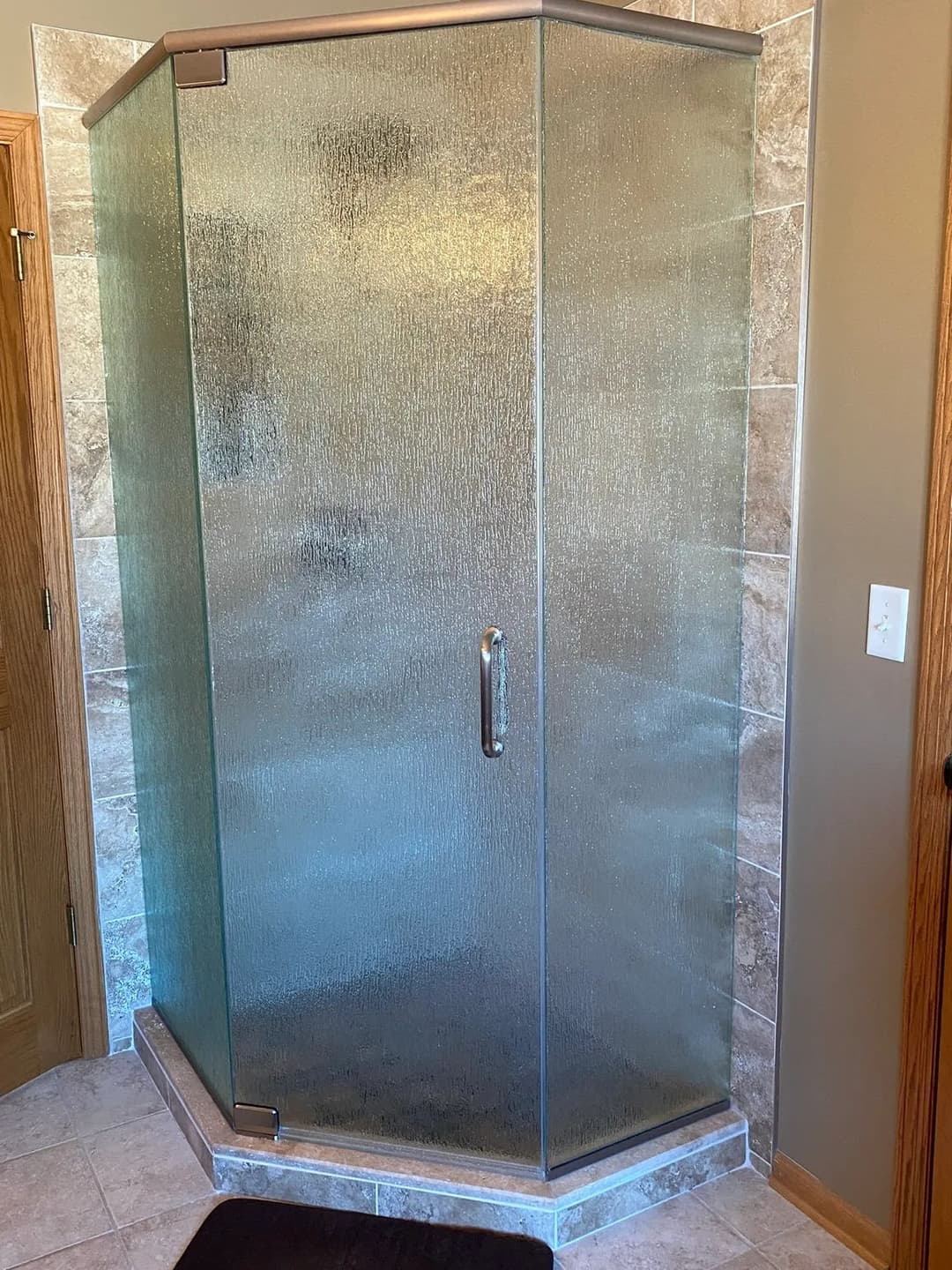 Frameless glass shower enclosure with textured panels in modern bathroom setting.