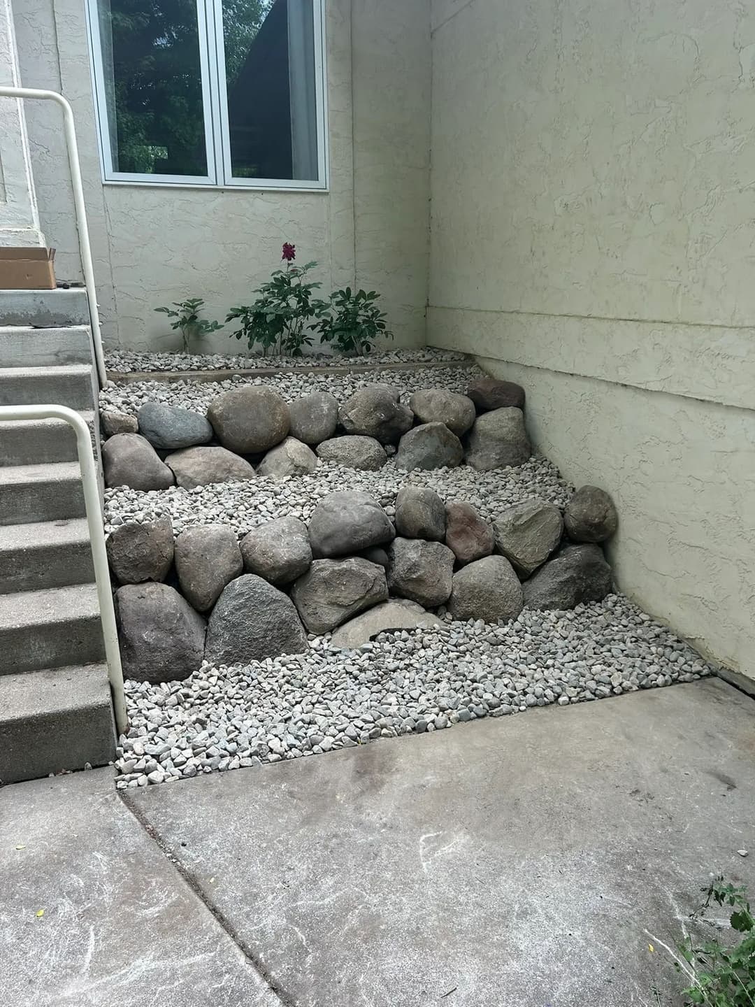 Rock garden with layered stone steps and a flowering plant near a building entrance.