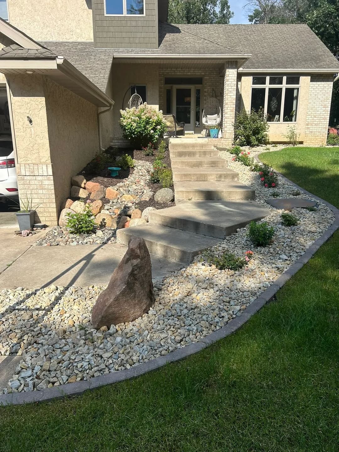 Landscape design featuring stone steps, shrubs, and a rock accent by a home's entrance.