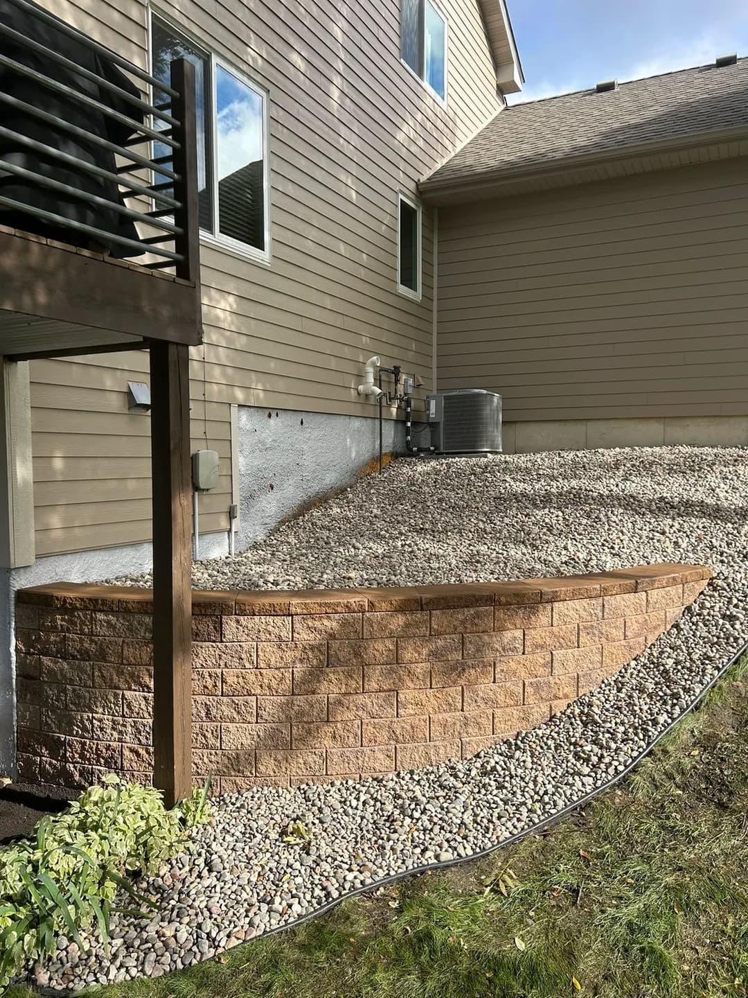 Stone retaining wall beside a house with gravel landscaping and air conditioning unit.