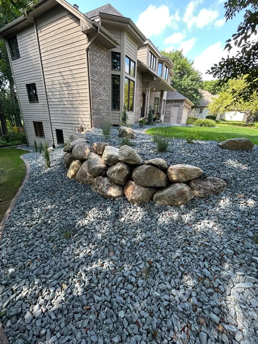 Landscaped yard featuring a rock formation and gravel near a modern home with large windows.