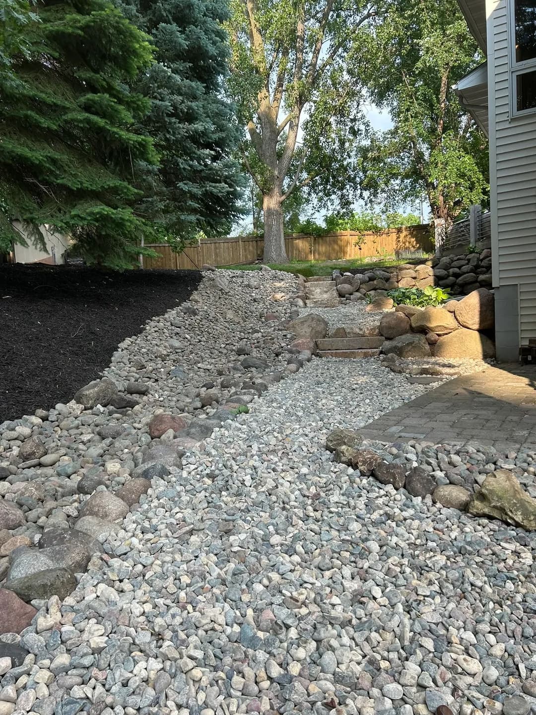 Rocky landscape path with stones leading to a lush green yard and trees. Garden design feature.