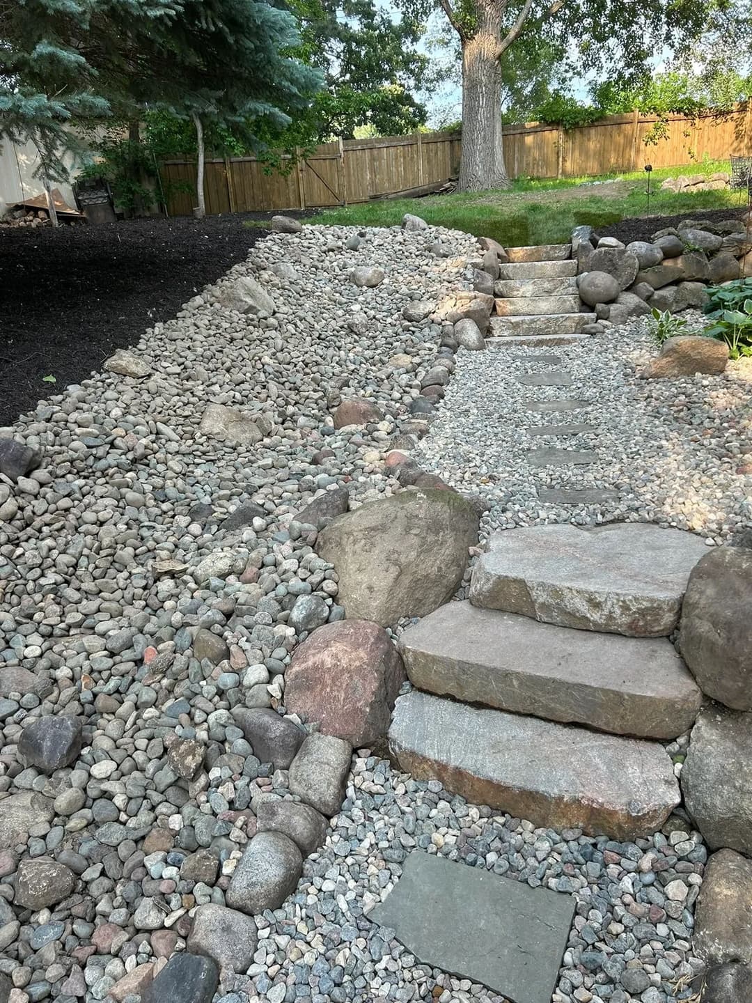 Stone pathway through landscaped garden with gravel and rocky edges.