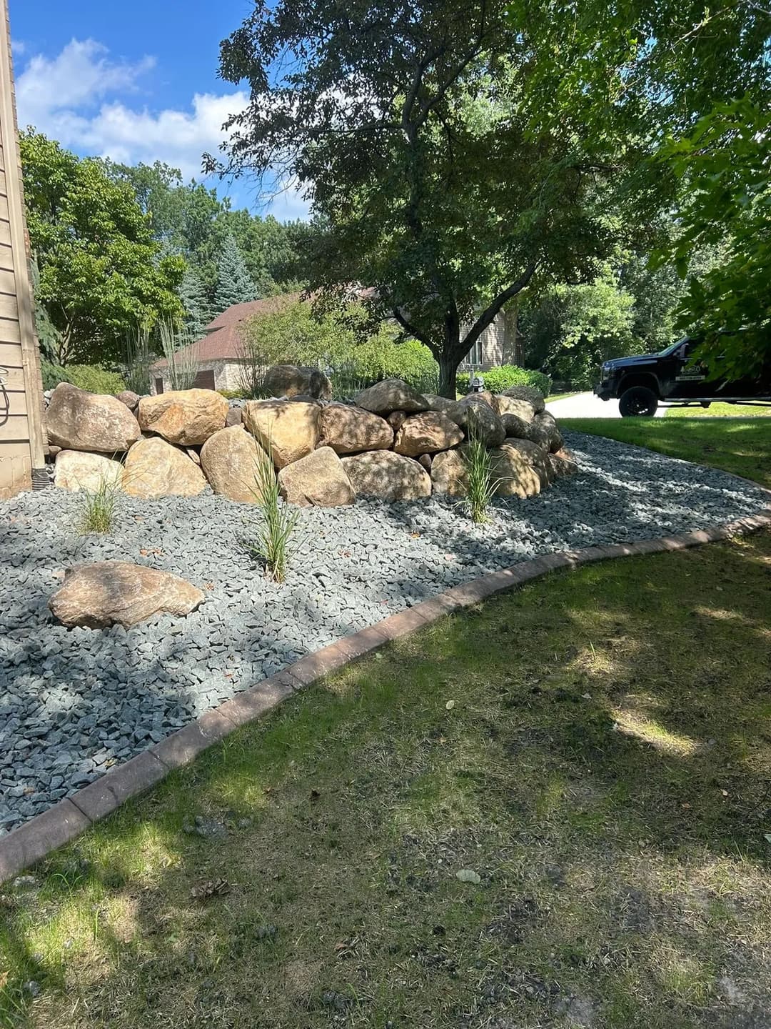 Landscape design featuring a stone rockery, gravel, and lush greenery near a home.
