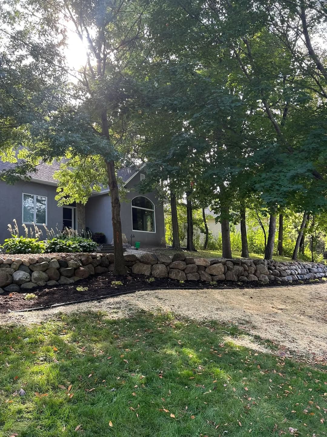 Beautiful home surrounded by trees and a stone wall in a serene garden setting.