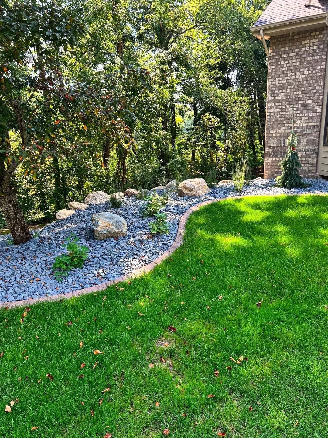 Lush green lawn with decorative stones and plants along a modern home landscape.