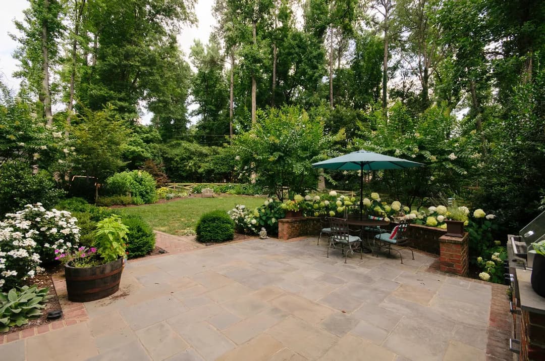 Lush garden patio with greenery, flowers, and an umbrella over a dining table.