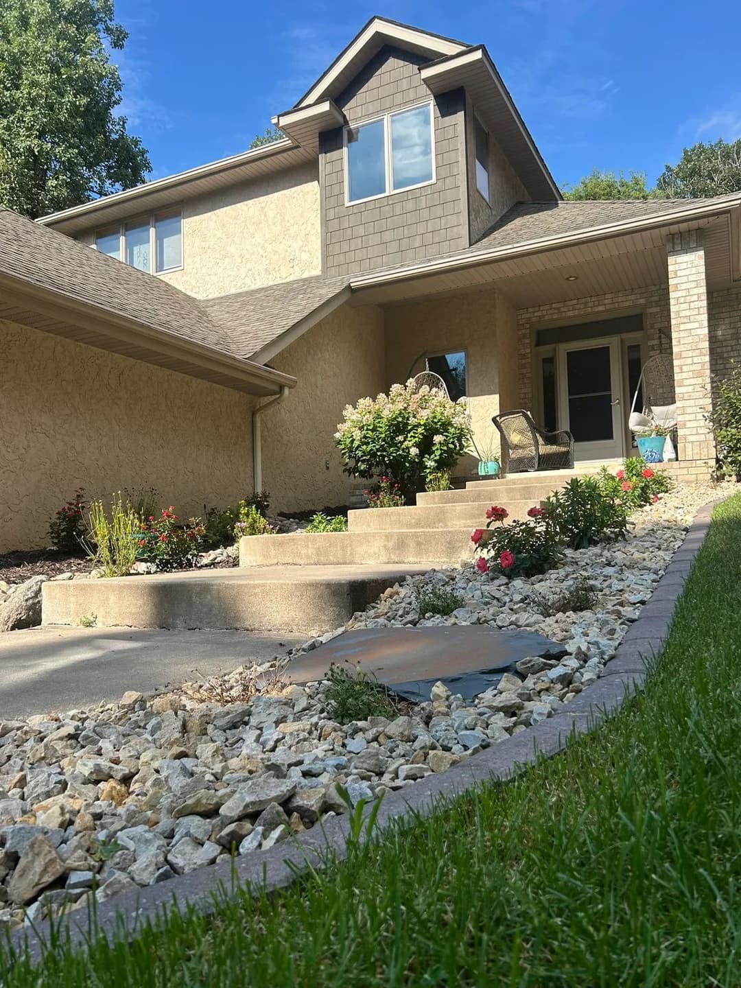Modern two-story house with landscaped front yard, flower beds, and stone pathway.