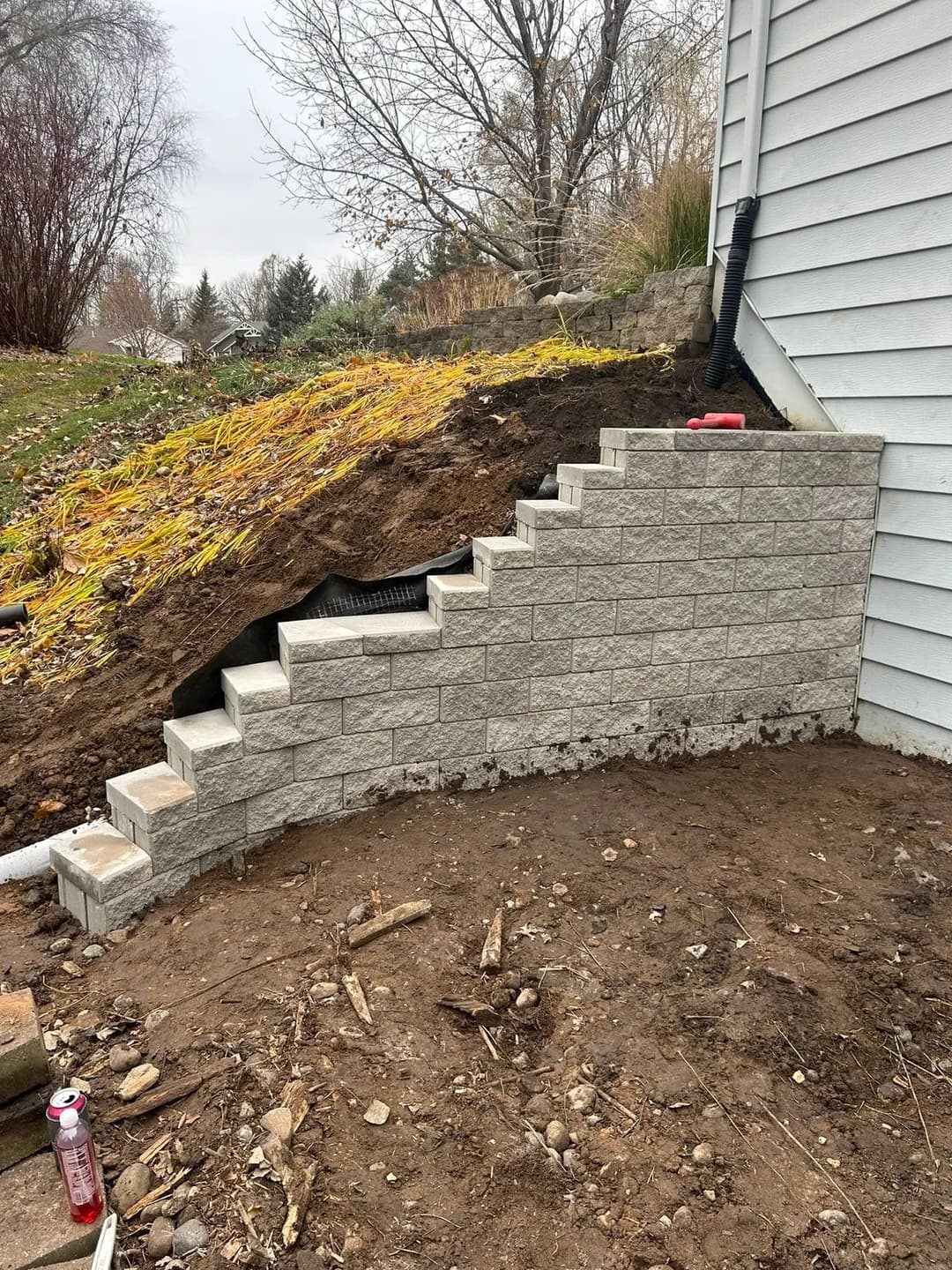 Gray stone steps leading up to a house, with a sloped yard and autumn foliage in the background.