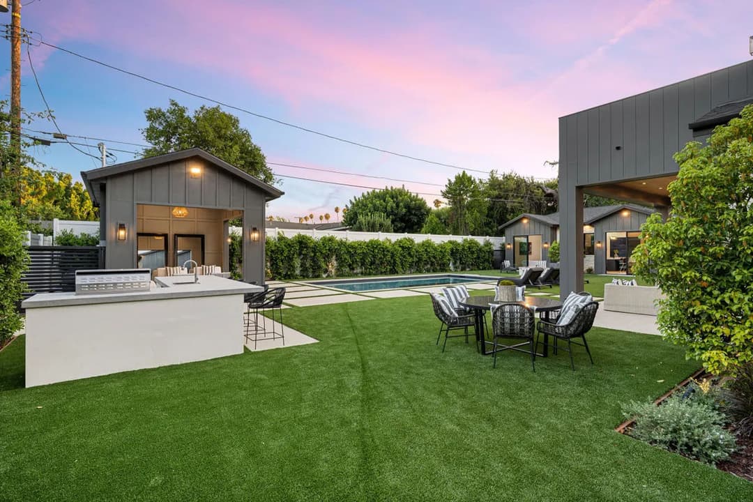 Modern backyard with pool, seating area, and outdoor kitchen under a colorful sunset.