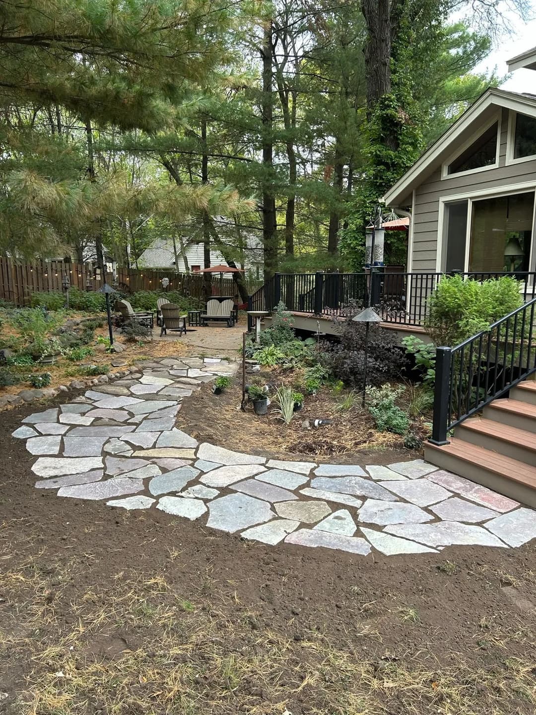 Stone pathway leading to a cozy backyard patio surrounded by greenery and trees.