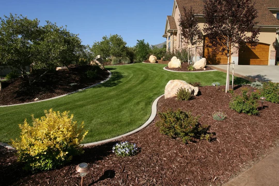Lush green lawn with landscaped flower beds and decorative rocks beside a home.
