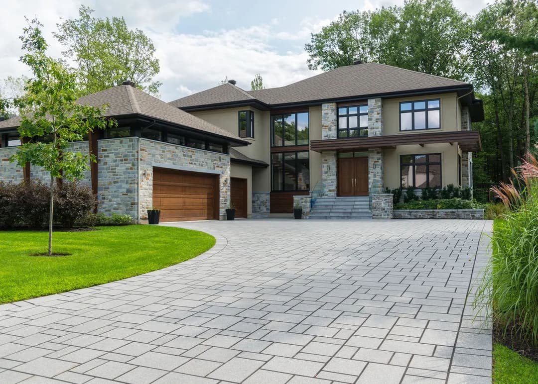 Modern luxury home with stone facade, landscaped driveway, and large windows.