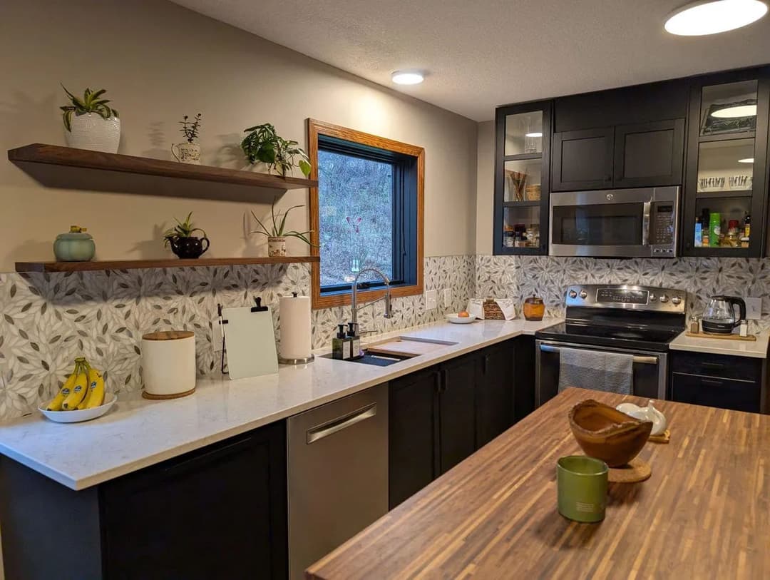 Modern kitchen with dark cabinets, patterned backsplash, and wooden countertop accents.